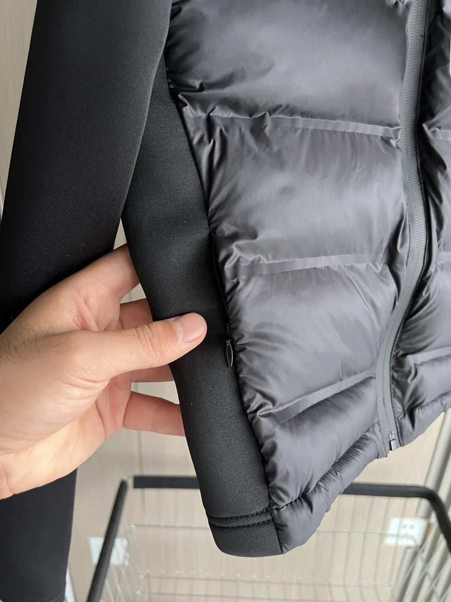 Close-up of hand holding black modern puffer jacket with quilted detail and front zipper