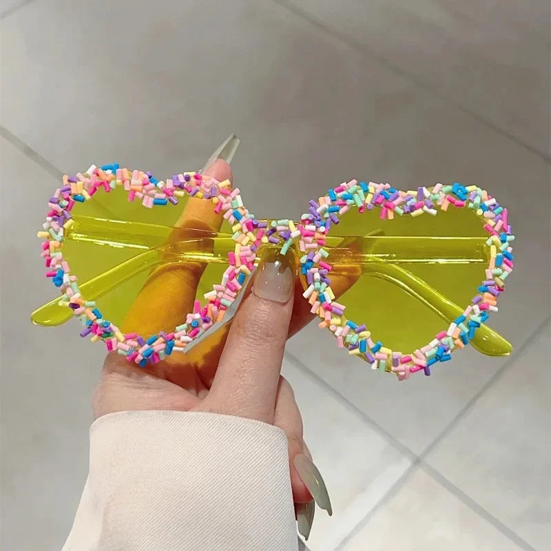 Yellow heart-shaped sunglasses with colorful sprinkle accents, held in hand