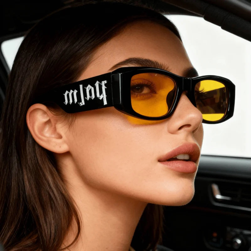 Woman wearing oversized black sunglasses with yellow lenses and white gothic lettering, modern fashion accessory
