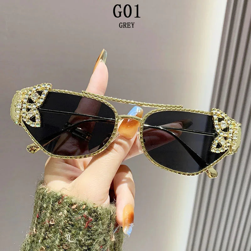 Gold-rimmed black sunglasses with rhinestone butterfly accents, held by hand