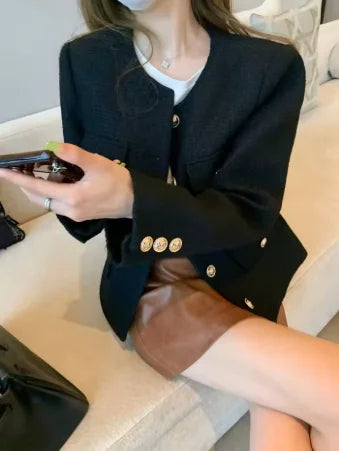 Woman wearing black blazer with gold buttons and brown leather skirt, sitting indoors