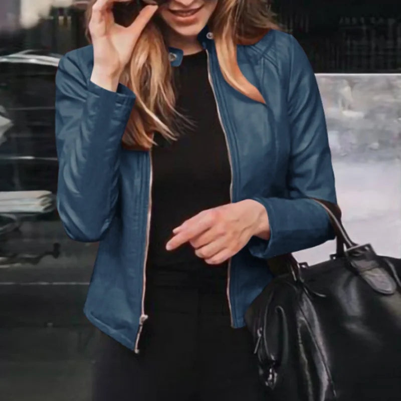 Woman wearing a blue faux leather jacket and black top, holding a stylish black handbag