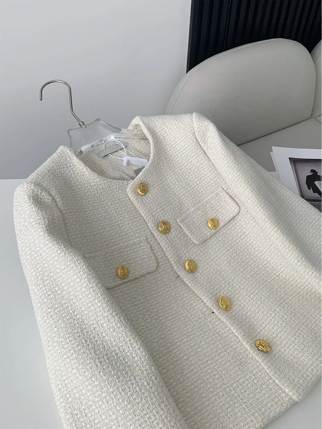 Elegant cream tweed jacket with gold buttons on a white chair, chic women's fashion