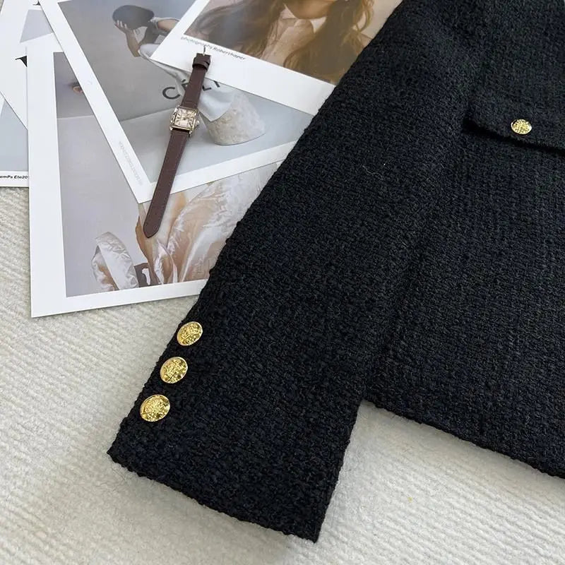 Black tweed blazer sleeve with gold buttons on a white surface, next to fashion magazines and a watch.